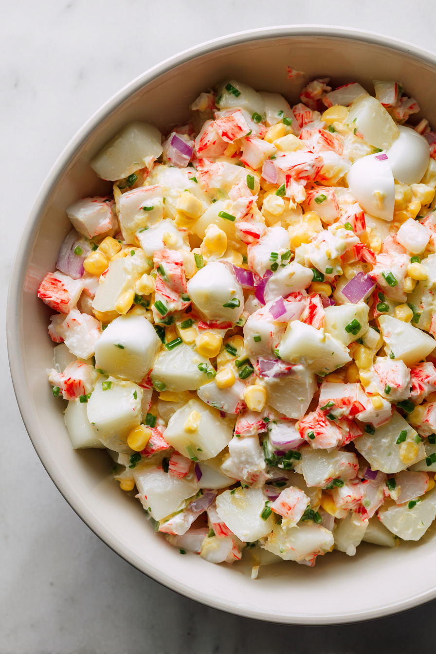 In a large mixing bowl, combine the chopped crab sticks, potatoes, eggs, corn, onions, and cooked rice.