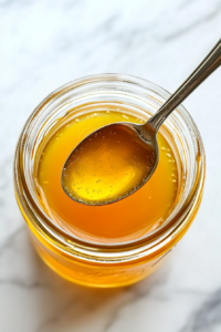 This image shows apple cider vinegar, lemon juice, and ground ginger being added to the honey and water mixture in a mason jar, getting ready to mix the healthy ingredients for the shots.