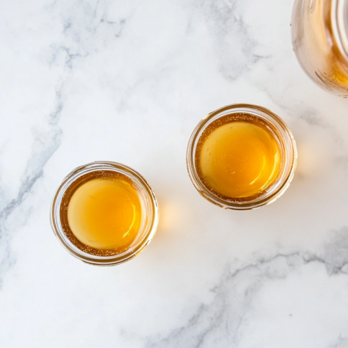 This image shows small shot glasses filled with apple cider vinegar shots, garnished with fresh lemon slices and ground ginger, ready to enjoy for a quick and healthy wellness boost.