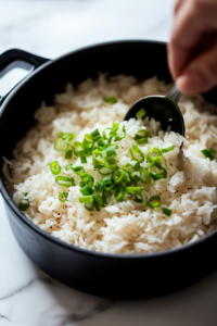 This image shows freshly sliced green onions being sprinkled over the cooked Asian rice, adding a fresh and slightly sharp garnish to balance the savory flavors.