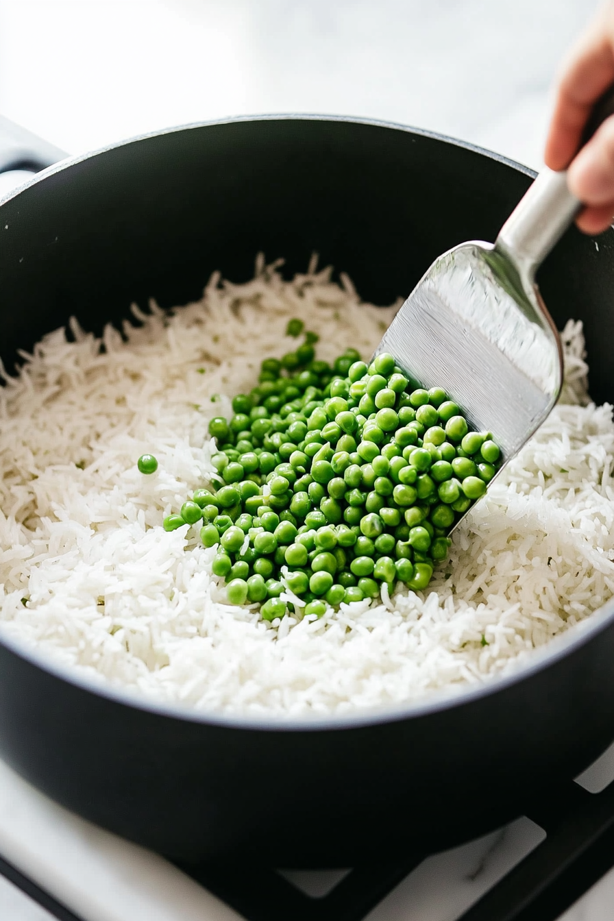 This image shows vibrant green frozen peas being mixed into the cooked rice, adding a pop of color and texture while heating through in the warm dish.