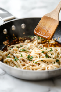 This image shows cooked noodles being tossed in a large frying pan with sautéed garlic, ginger, and the prepared sauce, illustrating the mixing process as the noodles absorb the delicious flavors.