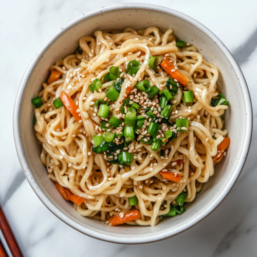 This image features a vibrant dish of Trader Joe’s squiggly noodles stir-fried with colorful vegetables and your choice of protein, topped with green onions and sesame seeds, making a visually appealing and delicious meal.