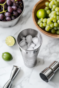 This image shows vodka, grape juice, and lime juice being poured into a cocktail shaker filled with ice, preparing to mix the Transfusion cocktail.