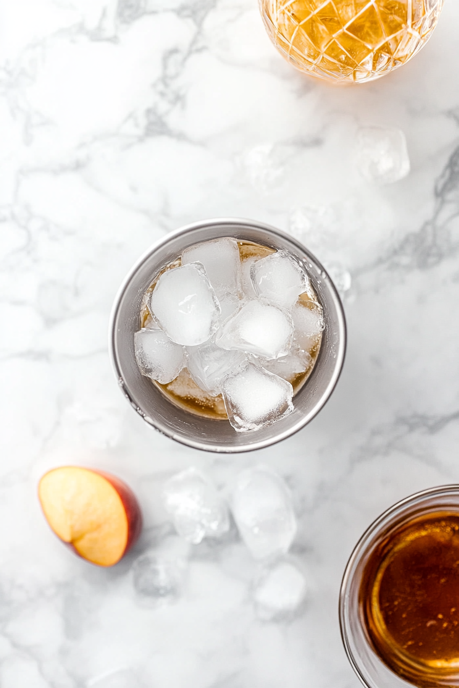 This image shows a cocktail shaker being filled with ice, whiskey, peach schnapps, and sour mix, preparing the ingredients for the Orange Tea Shot.