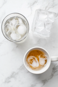 This image shows a glass being filled with ice cubes, ready to hold the chilled cortisol cocktail mixture for a refreshing and cooling effect.