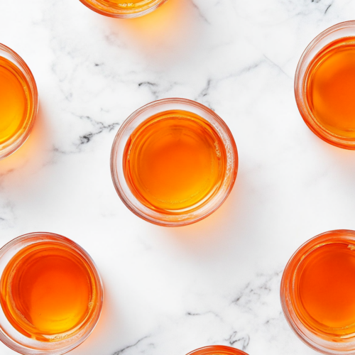 This image shows Orange Tea Shots served in small shot glasses, featuring a refreshing blend of whiskey, peach schnapps, sour mix, and optional lemon-lime soda for a vibrant, citrusy drink experience.