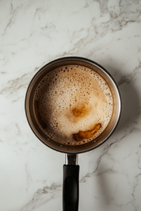 This image shows the leftover marinade of coconut aminos, honey, garlic, and ginger being boiled in a small saucepan to reduce into a savory glaze.