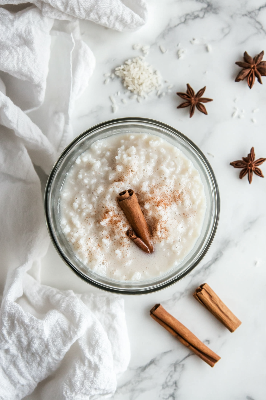 This image shows a mixing bowl filled with white rice, cinnamon sticks, and hot water, illustrating the soaking process as the ingredients blend together overnight to create a flavorful horchata.