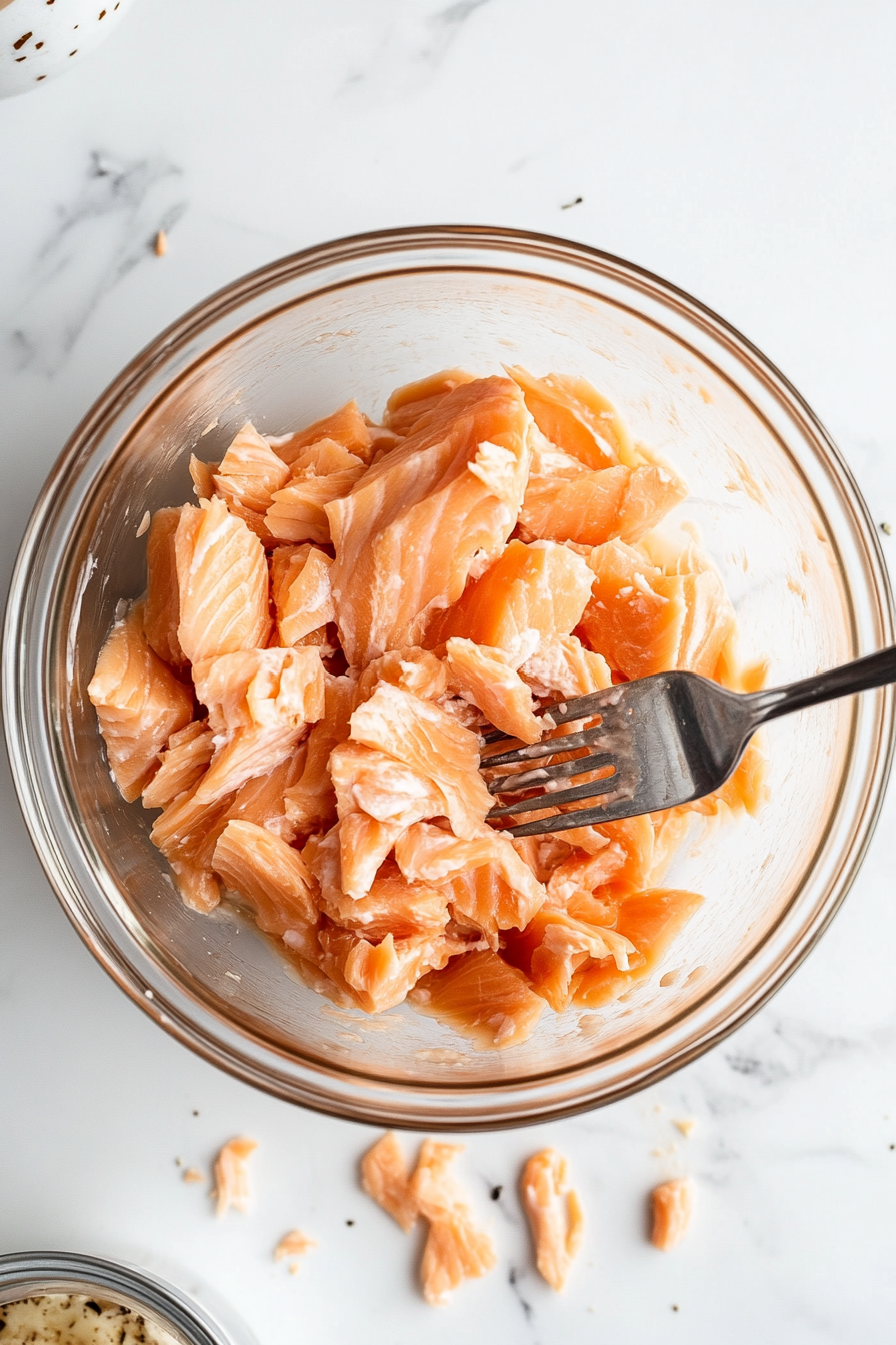 This image shows drained canned pink salmon in a mixing bowl being broken up with a fork, preparing it as the base for the Southern salmon patties mixture.