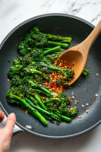 This image shows perfectly cooked broccolini, sprinkled with chili flakes, salt, and pepper, plated and ready to be served as a flavorful and healthy side dish.