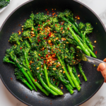 This image shows a vibrant plate of pan-fried broccolini, beautifully browned and garnished with garlic lemon seasoning, Parmesan cheese, and chili flakes for a crispy, flavorful finish.