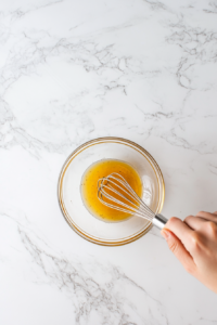 This image shows the preparation of a glaze, where honey, mustard, and olive oil are mixed together in a small bowl to create a flavorful coating for the gammon steaks.