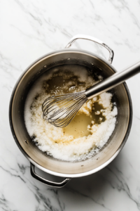 This image shows a pot filled with white vinegar, granulated sugar, pickling spice, and canning salt being heated to create the flavorful brine for sweet pickles.