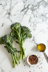 This image shows fresh broccolini being washed and trimmed, alongside olive oil and chili flakes, all set up to prepare a flavorful pan-fried broccolini dish.