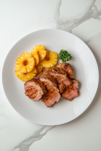 This image shows the finished gammon steaks served on a plate, crispy and juicy from the air fryer, alongside pineapple rings and chips, making for a delicious and easy meal.