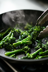 This image shows broccolini being pan-fried, with tongs stirring the florets as they turn golden-brown and slightly softened while cooking in olive oil.