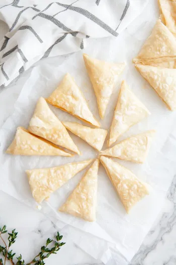 A baking sheet lined with parchment paper on a white marble cooktop, with the oven preheated to 375°F. A digital thermometer shows the correct temperature. The scene sets the stage for baking crescent rolls.