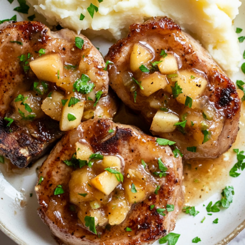 This image shows the beautifully plated apple chutney pork chops, paired with creamy mashed potatoes and garnished with freshly chopped parsley, making for a comforting and flavorful meal.