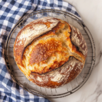 This image shows the finished cinnamon swirl apple fritter bread, drizzled with a sweet glaze and garnished with a light dusting of cinnamon, ready to be sliced and served. The golden crust and juicy apple chunks are visible, showcasing the delicious and comforting flavors of this autumn-inspired bread.