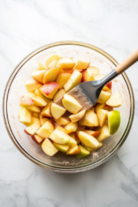 This image shows diced Granny Smith apples being evenly coated with a mixture of cinnamon and sugar, enhancing the apples with a warm and sweet flavor before they are layered into the bread.