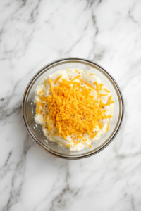 This image displays the addition of grated pepper jack cheese, sharp cheddar cheese, minced onion, minced garlic, Worcestershire sauce, and Tabasco sauce to the creamy mixture, creating a flavorful and cheesy base for the Cold Crab Dip.