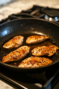 This image shows the seasoned chicken cooking in a hot skillet, turning golden brown on the outside as it sears, locking in flavor and juices.