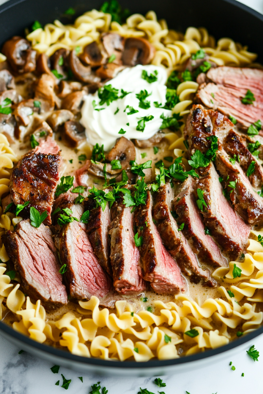 This image shows sour cream being stirred into the stroganoff sauce and slices of leftover prime rib added to the pan, ready to be served over freshly cooked noodles.