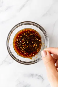 This image shows the cook adjusting the thickness of the dipping sauce by adding additional hoisin sauce. The sauce is thickening slightly as the ingredients are stirred to a rich consistency.