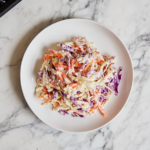 This image shows a vibrant bowl of vegan coleslaw, featuring shredded red cabbage and carrots tossed in a creamy, tangy vegan mayo and apple cider vinegar dressing, perfect for a refreshing side dish.