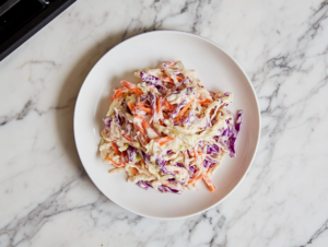 This image shows a vibrant bowl of vegan coleslaw, featuring shredded red cabbage and carrots tossed in a creamy, tangy vegan mayo and apple cider vinegar dressing, perfect for a refreshing side dish.