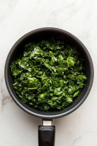 This image shows spinach being cooked in a saucepan until soft and wilted, preparing the base for the vibrant Palak Sauce.