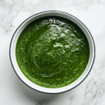 This image shows a bowl of creamy and smooth Palak Sauce, topped with a sprinkle of fresh herbs, showcasing its rich green color and inviting texture. Perfect for pairing with Indian dishes.