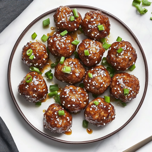 This image shows a platter of tender and juicy Asian meatballs, glistening with a flavorful sauce, and garnished with fresh green onions and sesame seeds, making it a perfect appetizer for any occasion.