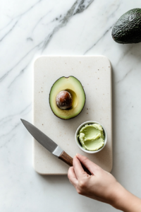 This image shows the process of slicing a ripe avocado in half and removing the pit, readying it for mashing to spread on toast.