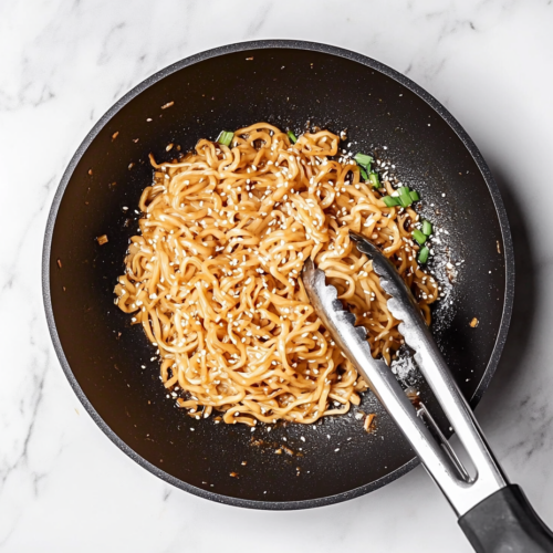 This image shows a bowl of freshly made Teriyaki Noodles, garnished with thinly sliced green onions and sprinkled with sesame seeds, ready to be enjoyed as a flavorful and satisfying meal.