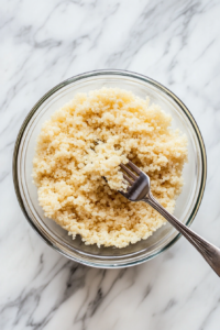 This image shows quinoa being fluffed with a fork after cooking. The grains appear light and airy, perfect for serving as a side dish or base for various meals.