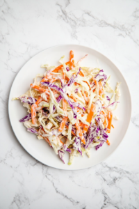 This image shows a vibrant bowl of vegan coleslaw, featuring shredded red cabbage and carrots tossed in a creamy, tangy vegan mayo and apple cider vinegar dressing, perfect for a refreshing side dish.