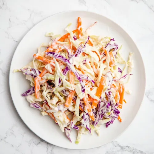 This image shows a vibrant bowl of vegan coleslaw, featuring shredded red cabbage and carrots tossed in a creamy, tangy vegan mayo and apple cider vinegar dressing, perfect for a refreshing side dish.