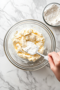 This image shows the process of gently folding sifted flour and baking powder into the light egg mixture using a spatula, carefully combining the ingredients for a smooth Nutella rolls batter.