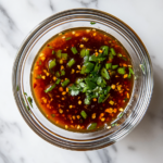 This image shows a bowl of light and flavorful spring roll dipping sauce, made with a blend of soy, hoisin, garlic, ginger, and sesame oil, served alongside fresh, vibrant spring rolls. The sauce looks rich and perfect for enhancing the taste of the rolls.