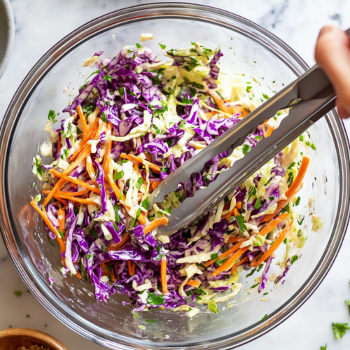 This image shows a colorful bowl of Mexican street slaw made with shredded cabbage, charred corn, jalapeños, and a tangy lime dressing. The slaw is garnished with fresh cilantro and crumbled feta cheese, perfect for serving as a fresh and zesty side dish.