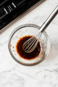 This image shows a small bowl with hoisin sauce, soy sauce, rice vinegar, and sesame oil being mixed together to create a flavorful sauce for the tofu filling in the vegan lettuce wraps.