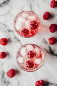 This image shows chilled club soda being poured over ice cubes into the raspberry syrup-filled glasses, creating a fizzy and refreshing base for the Italian soda.