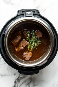 This image shows the chuck roast in the Instant Pot, fully submerged in a rich beef broth, rosemary, and soy sauce, ready to be pressure-cooked to tenderness.