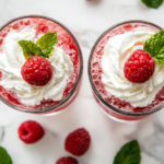 This image shows a beautifully served raspberry Italian soda in a tall glass, topped with fluffy whipped cream, fresh raspberries, and a mint sprig, creating a vibrant and refreshing summer drink.