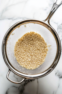 This image shows quinoa being rinsed under cold water in a fine mesh strainer. The rinsing process removes bitterness and prepares the quinoa for cooking in the microwave.