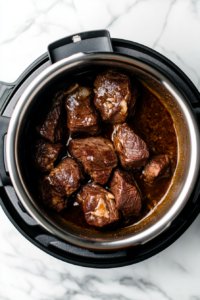 This image shows the chuck roast being browned on all sides in an Instant Pot set to sauté mode, creating a rich golden crust that adds flavor to the French dip sandwich.