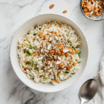 This image shows the completed ramen noodle salad served in a bowl, topped with toasted ramen noodles, sunflower seeds, almonds, and a drizzle of tangy dressing, ready to be enjoyed as a refreshing side dish.