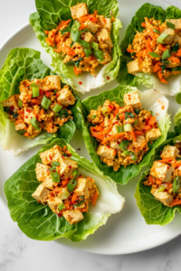 This image shows the tofu and mushroom mixture being spooned into large romaine lettuce leaves, ready to be topped with grated carrots and green onions.